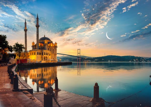 Die beleuchtete Ortaköy-Moschee in Istanbul bei Sonnenaufgang mit einer Brücke im Hintergrund.