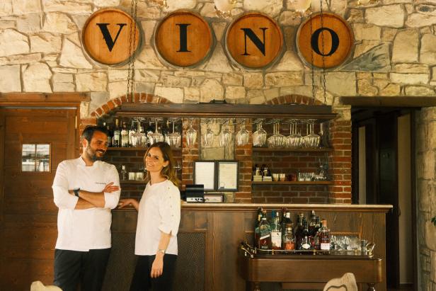 Ein Koch und eine Frau stehen vor einer Bar mit der Aufschrift „VINO“.