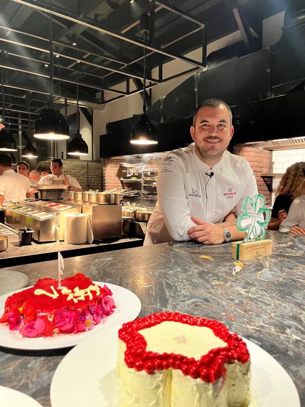 Ein Koch steht in einer Küche vor zwei verzierten Kuchen und einer Michelin-Auszeichnung.