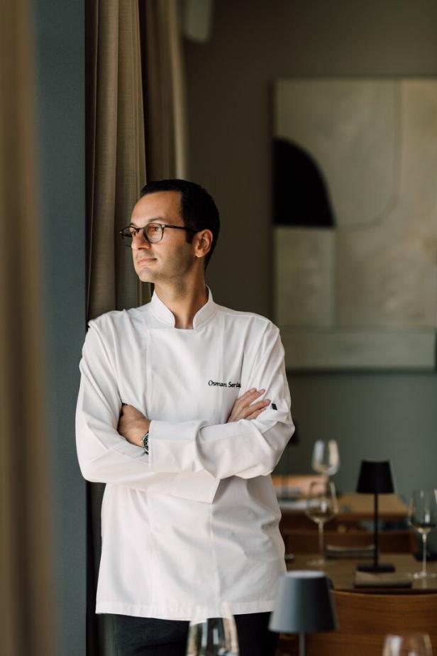 Ein Koch namens Osman Serdar steht mit verschränkten Armen in einem Restaurant und blickt aus dem Fenster.