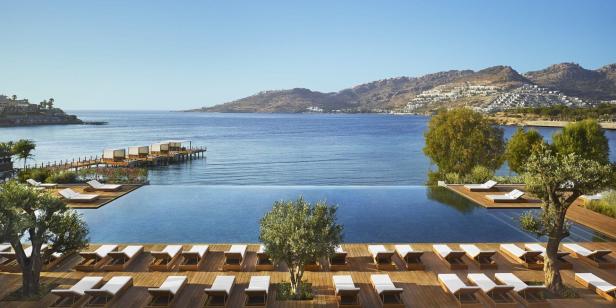 Ein Infinity-Pool mit Liegestühlen bietet einen Blick auf das Meer und die Küstenlandschaft.