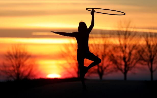 Eine Frau trainiert mit einem Hula-Hoop-Reifen vor einem Sonnenuntergang.