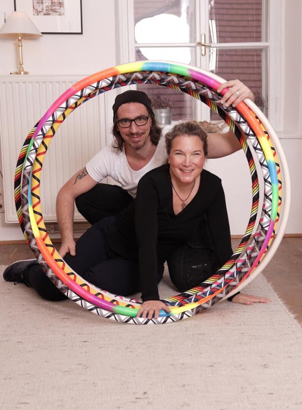Ein Mann und eine Frau knien auf einem Teppich, umgeben von bunten Hula-Hoop-Reifen.