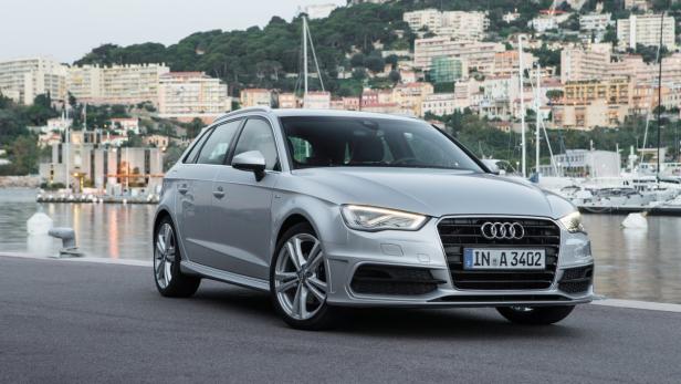 Ein silberner Audi A3 steht vor einer Stadt am Wasser.