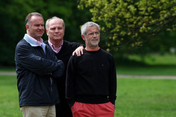 Drei Männer stehen im Freien vor einem Baum mit grünen Blättern.