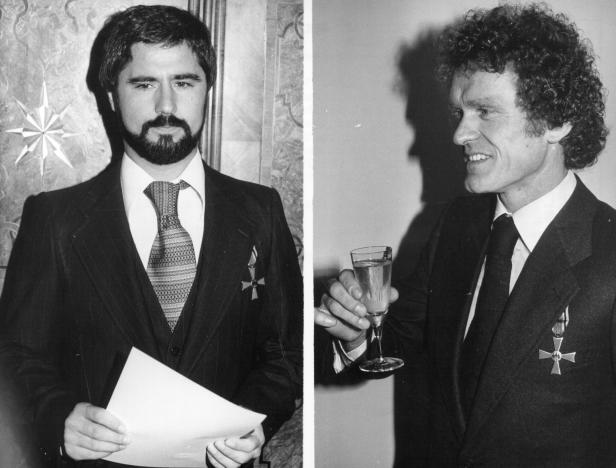 Zwei Männer in Anzügen, einer mit einem Glas in der Hand, tragen Orden.