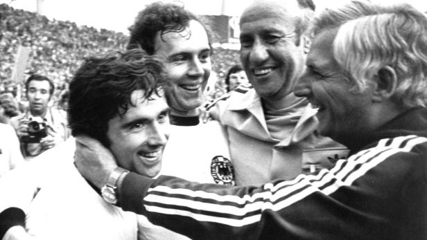 Deutsche Fußballspieler und ihr Trainer umarmen sich freudig.