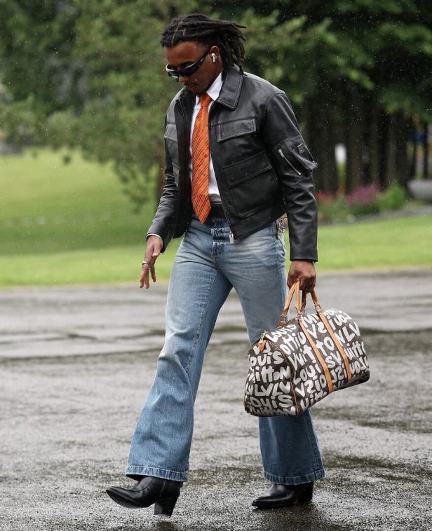 Ein Mann mit Sonnenbrille und Louis-Vuitton-Tasche geht im Regen.