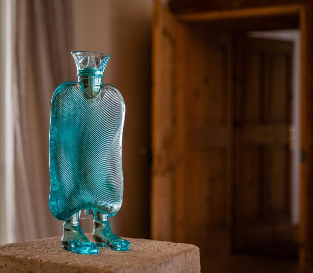 Eine blaue Glas-Skulptur im Stil von Erwin Wurm steht auf einem Sockel.