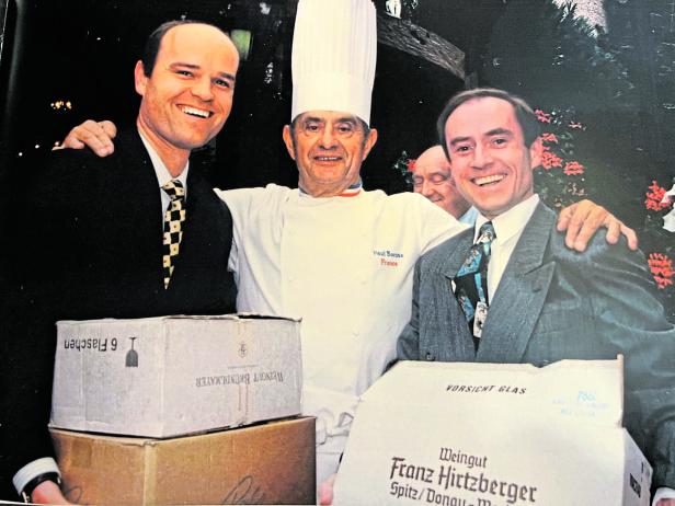 Koch Paul Bocuse mit zwei Männern, die Weinkartons der Weingüter Brundlmayer und Hirtzberger halten.