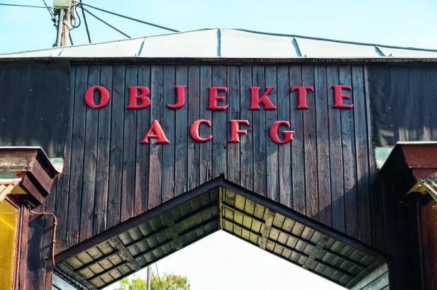 Eine hölzerne Überdachung am Eingang des Strombads Kritzendorf. Darauf steht als Zugang zu den Kästchen „Objekte ACFG“.