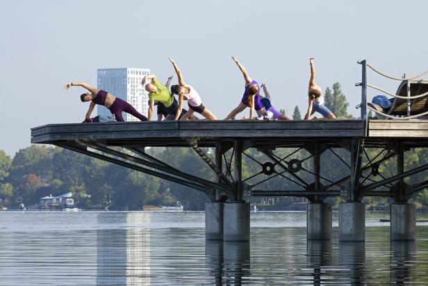 Eine Gruppe von Menschen macht Yoga auf einer Plattform über dem Wasser.