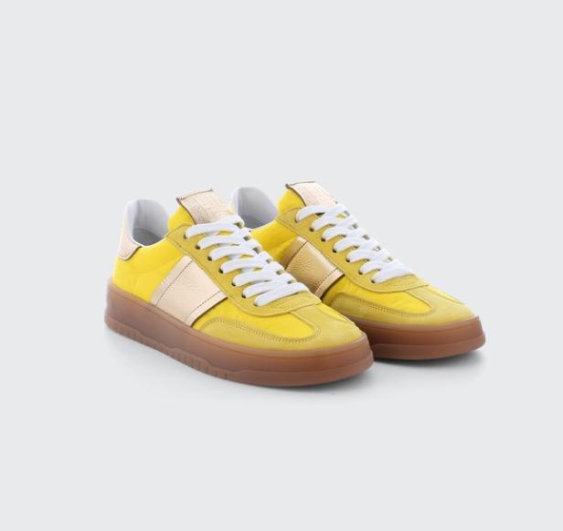 Ein Paar gelbe Sneaker mit goldenen Streifen und weißen Schnürsenkeln stehen auf einem weißen Hintergrund.