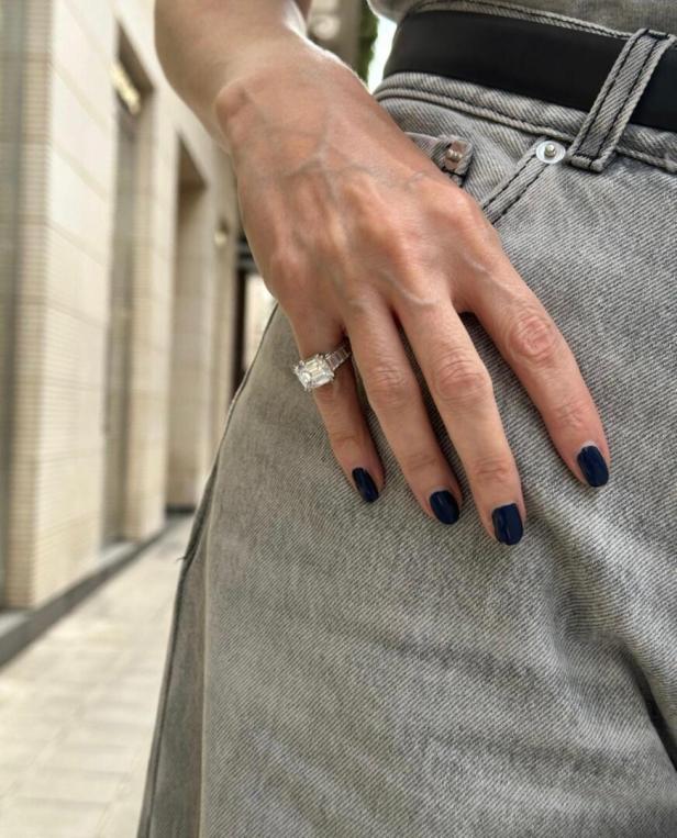 Die Hand einer Person mit einem großen Diamantring auf grauem Jeansstoff.