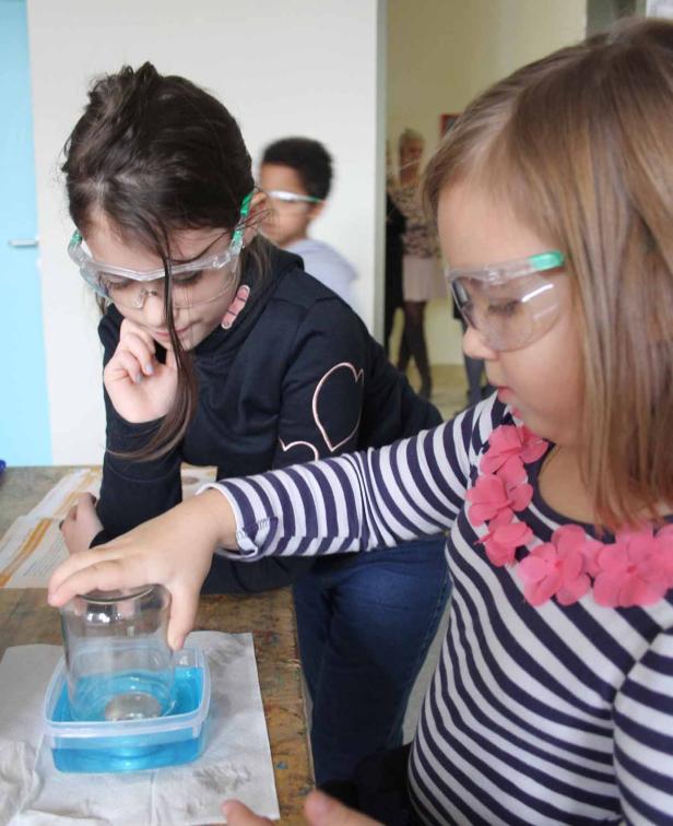 Zwei Mädchen mit Schutzbrillen führen ein Experiment mit Wasser durch.
