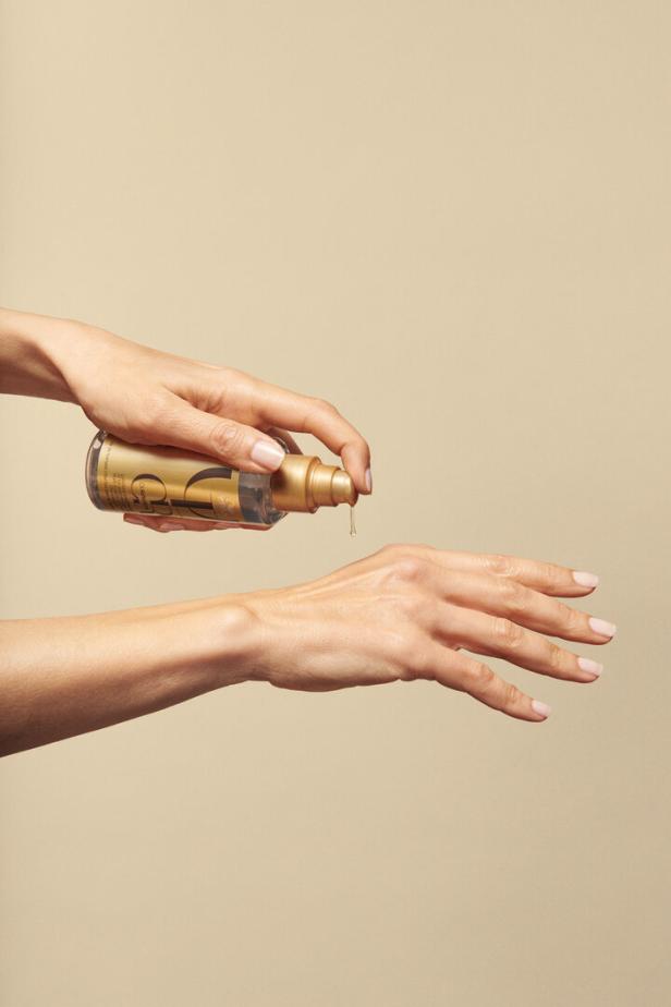 Eine Person träufelt Öl aus einer goldenen Flasche auf ihren Handrücken.