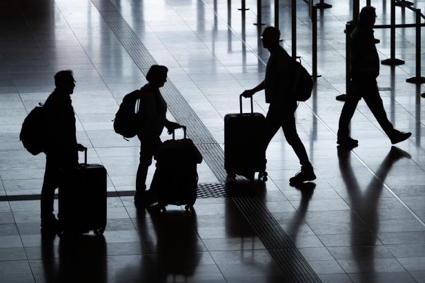 Silhouetten von Reisenden mit Gepäck in einem hellen Terminal.
