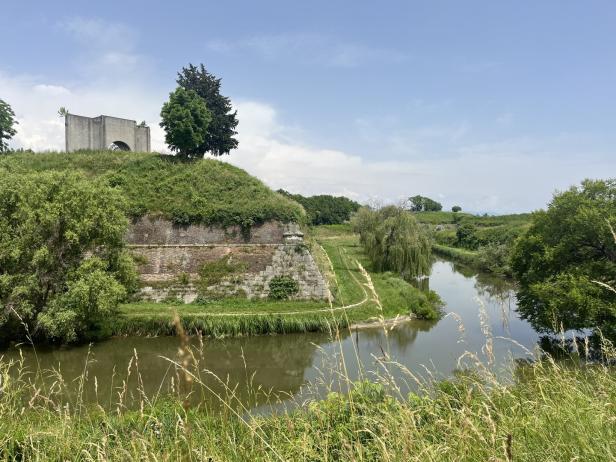 Ein Wassergraben umgibt einen grasbewachsenen Hügel mit einem alten Gebäude darauf.