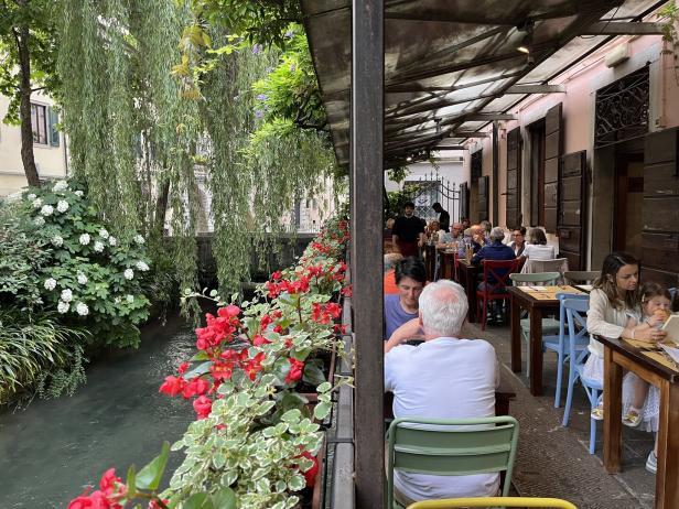 Ein Restaurant am Wasser mit blühenden Blumen und Gästen an den Tischen.