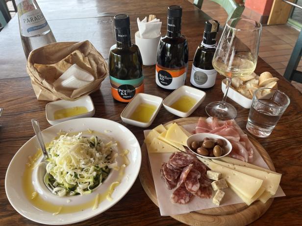 Ein Tisch mit Olivenöl, Käse, Salami, Brot und einem Zucchini-Gericht.