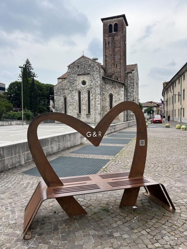 Eine herzförmige Bank steht vor einer Kirche in Cividale del Friuli, Italien.