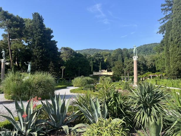 Ein formeller Garten mit Statuen und üppiger Vegetation an einem sonnigen Tag.