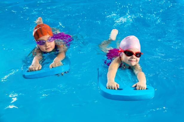 Zwei Mädchen schwimmen mit Schwimmbrettern im Wasser.