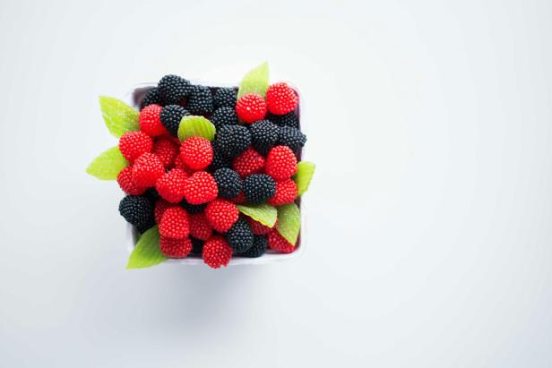 Ein Behälter gefüllt mit roten und schwarzen Gummibärchen in Form von Beeren und grünen Blättern.