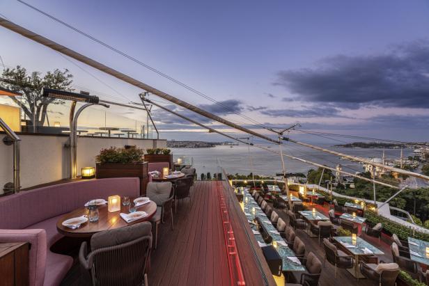 Ein Restaurant mit Tischen und Stühlen bietet einen Panoramablick auf das Meer bei Sonnenuntergang.