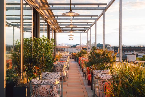Ein Dachterrassen-Restaurant mit Pflanzen, Sonnenschirmen und Blick auf die Stadt.