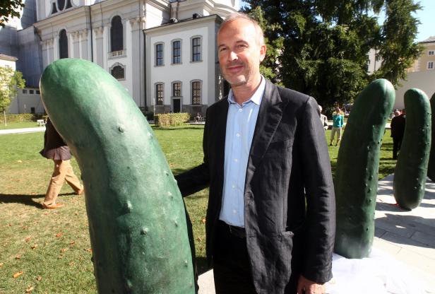 Ein Mann posiert neben einer Gurken-Skulptur im Freien.