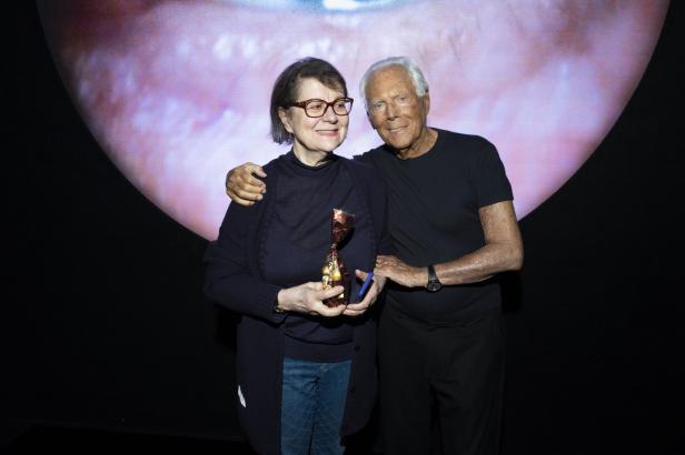 Giorgio Armani umarmt eine Frau, die eine Auszeichnung hält.