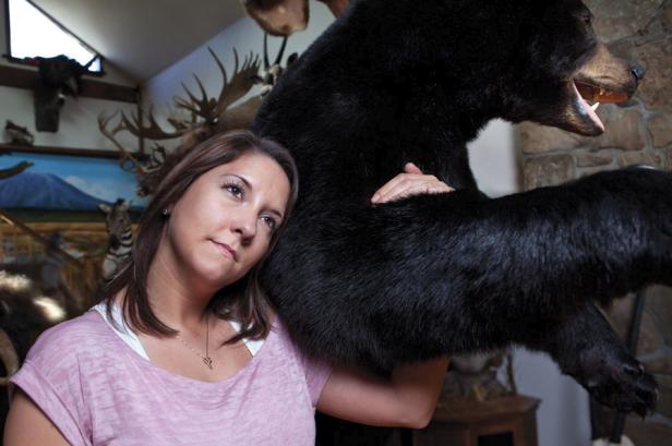 Eine Frau lehnt an einem ausgestopften Bären in einem Raum mit Jagdtrophäen.