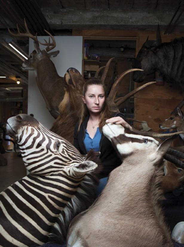 Eine Frau posiert inmitten von ausgestopften Tieren, darunter ein Zebra, ein Hirsch und verschiedene Antilopen.