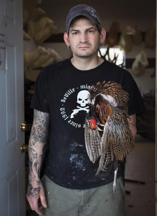 Ein Mann mit Tätowierungen hält einen toten Vogel in seinen Händen.