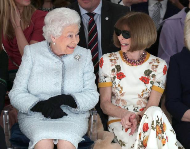 Königin Elisabeth II. und Anna Wintour sitzen nebeneinander bei einer Modenschau.