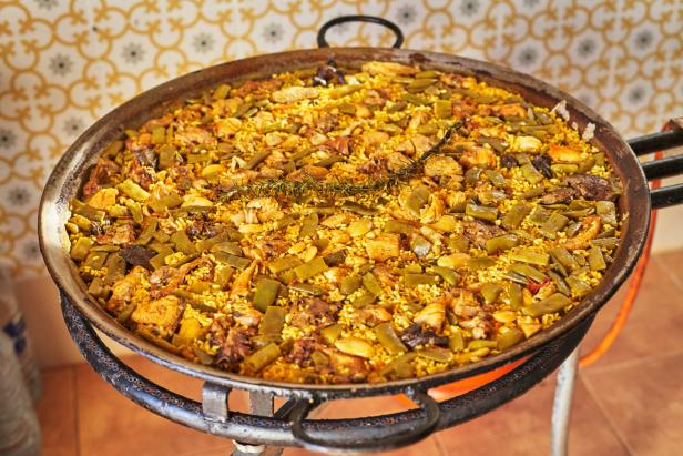 Eine Paella mit Reis, grünen Bohnen und Fleisch wird auf einem Gasbrenner zubereitet.