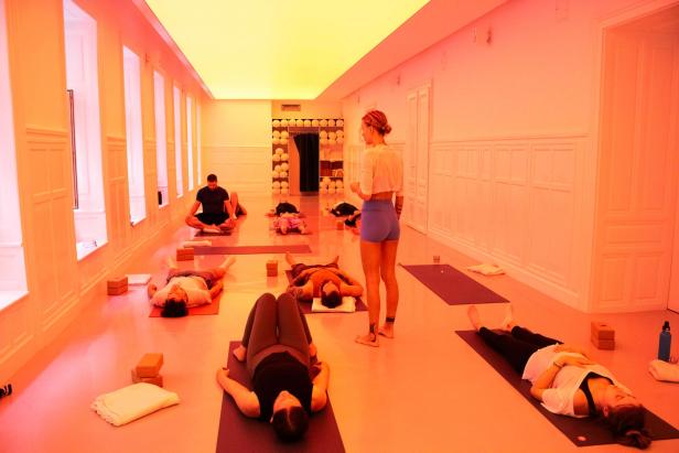 In einem Yogastudio entspannen sich mehrere Personen auf Yogamatten, während eine Lehrerin steht.