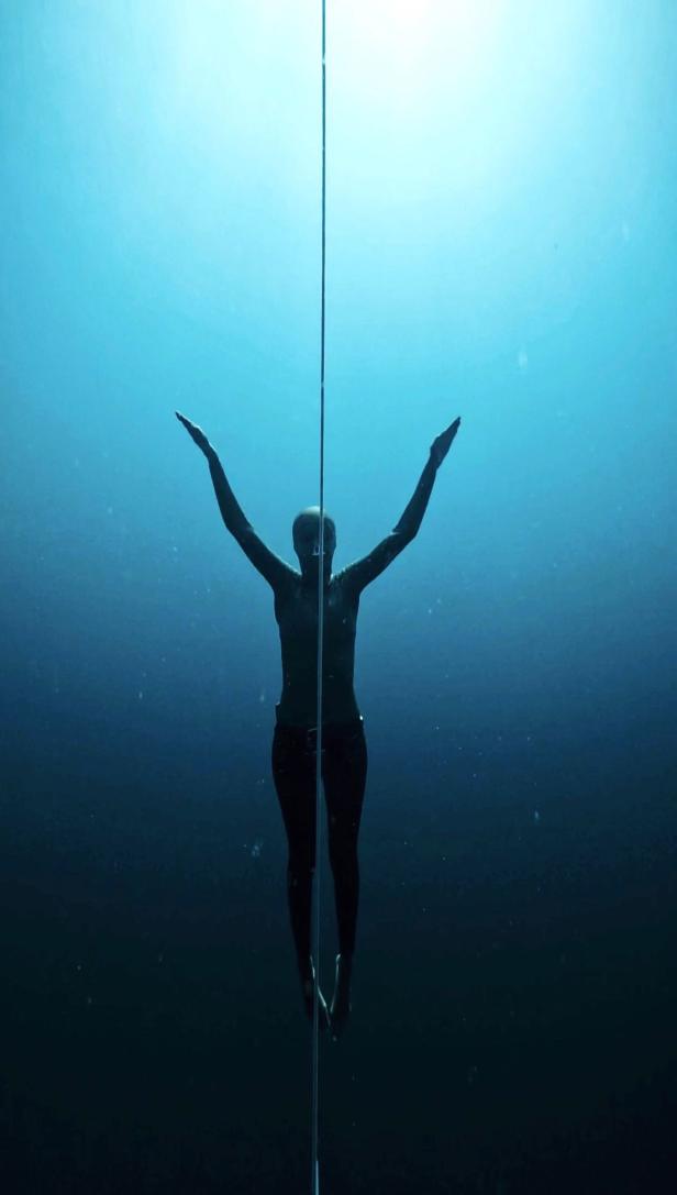 Eine Frau taucht mit erhobenen Armen an einem Seil im tiefen, blauen Wasser.