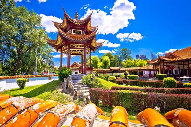 Ein chinesischer Pavillon steht in einem gepflegten Garten unter blauem Himmel.