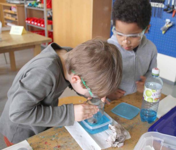 Zwei Kinder beobachten ein Experiment mit Wasser und einem Glasbehälter.