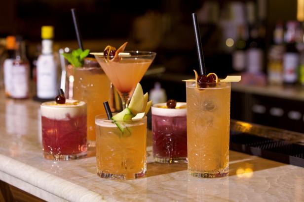 Mehrere bunte Cocktails stehen auf einer Bar.