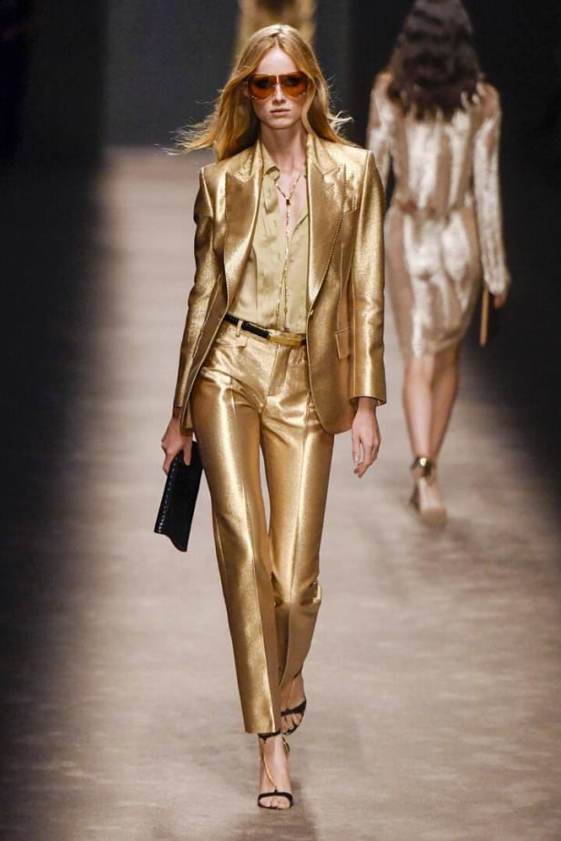 Eine Frau in einem goldenen Hosenanzug auf einem Laufsteg.