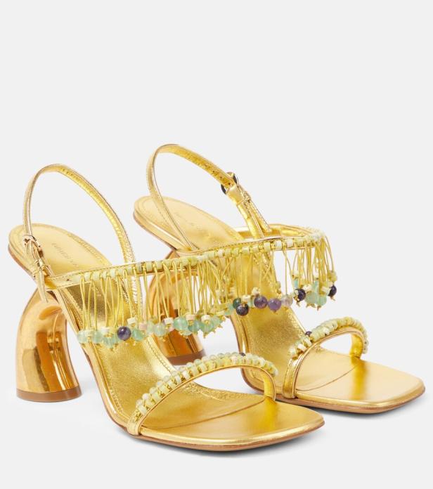 Ein Paar goldene Sandalen mit Absatz und Fransen mit bunten Perlen.