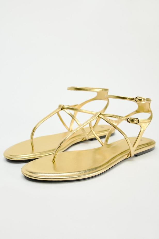 Ein Paar goldene Sandalen mit Riemchen stehen vor einem weißen Hintergrund.