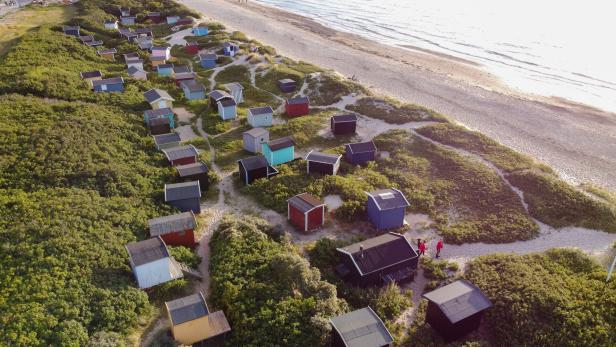 Luftaufnahme von bunten Strandhäusern in einer Dünenlandschaft am Meer.