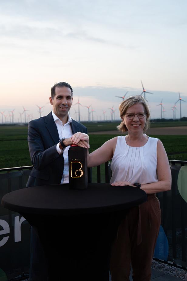 Zwei Personen stehen an einem Tisch mit Windrädern im Hintergrund.