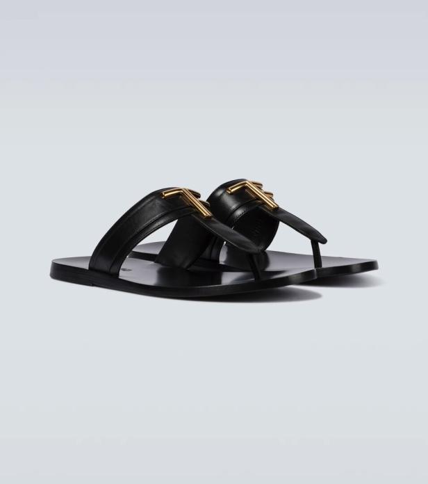 Ein Paar schwarze Ledersandalen mit goldenen Schnallen stehen auf einem hellen Untergrund.
