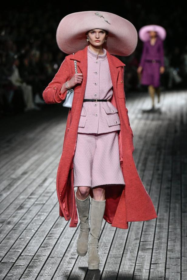 Eine Frau mit einem großen rosa Hut und einem passenden Ensemble auf einem Laufsteg.