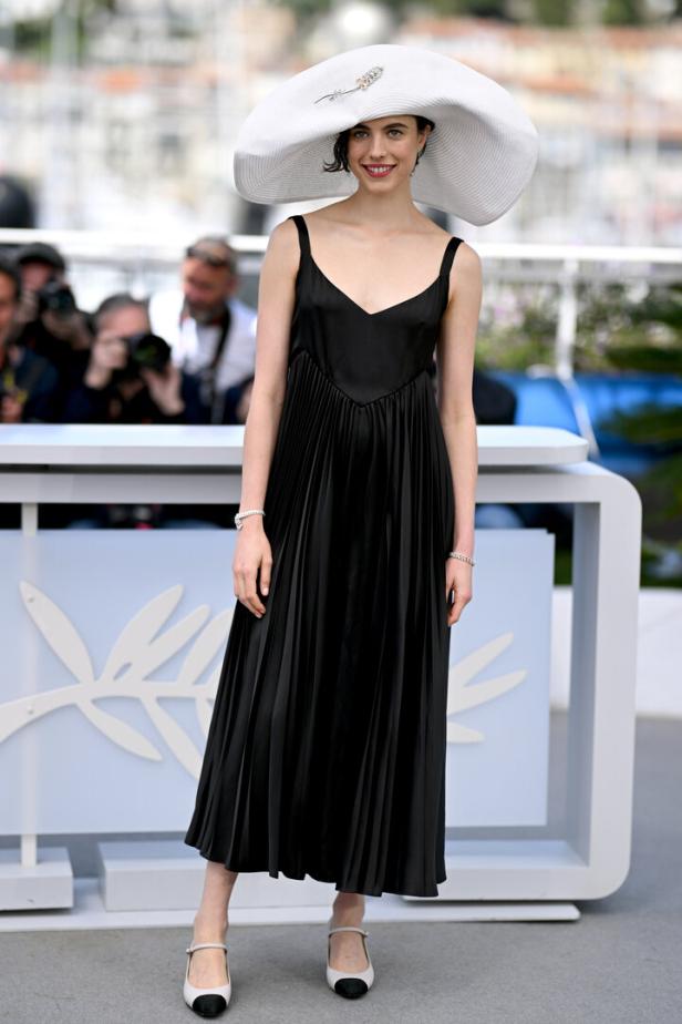 Margaret Qualley trägt ein schwarzes Kleid und einen großen weißen Hut.